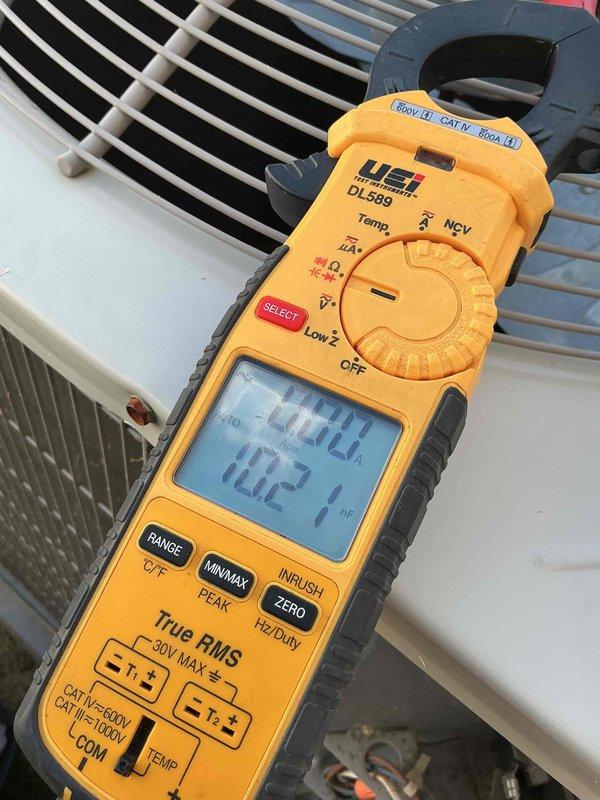 Responded to no cooling complaint on 2017 system. Upon arrival, found unit not operating efficiently with warm copper line at indoor coil indicating potential compressor or refrigerant issue. Performed diagnostic testing of outdoor unit components including amperage draw measurements using clamp meter, which revealed readings of approximately 70 amps. Inspected dual-run capacitor rated at 40/5 μF 440VAC, noting visible wear and discoloration on housing. Capacitor showed signs of age-related deterioration with accumulated debris on mounting surface. Documented electrical measurements and component conditions with photos for service records. Advised customer of findings and provided recommendations for necessary repairs to restore proper cooling operation.