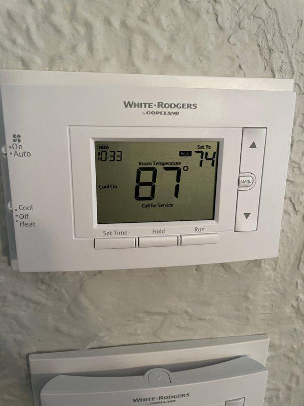 Completed HVAC system installation including air handler unit with 5KW heat kit, drain pan, and wet switch safety device. Installed two programmable White-Rodgers thermostats, new electrical disconnect with whip, 25x25 return air filter grill, and PVC condensate drain lines with proper trap configuration. Verified electrical service with correct breaker sizing and wire gauge for system requirements. Documentation photos captured for utility rebate program showing thermostat installation displaying 87°F room temperature with system calling for cooling at 74°F setpoint, and attic-mounted air handler with flexible ductwork and condensate drainage system properly installed on platform.