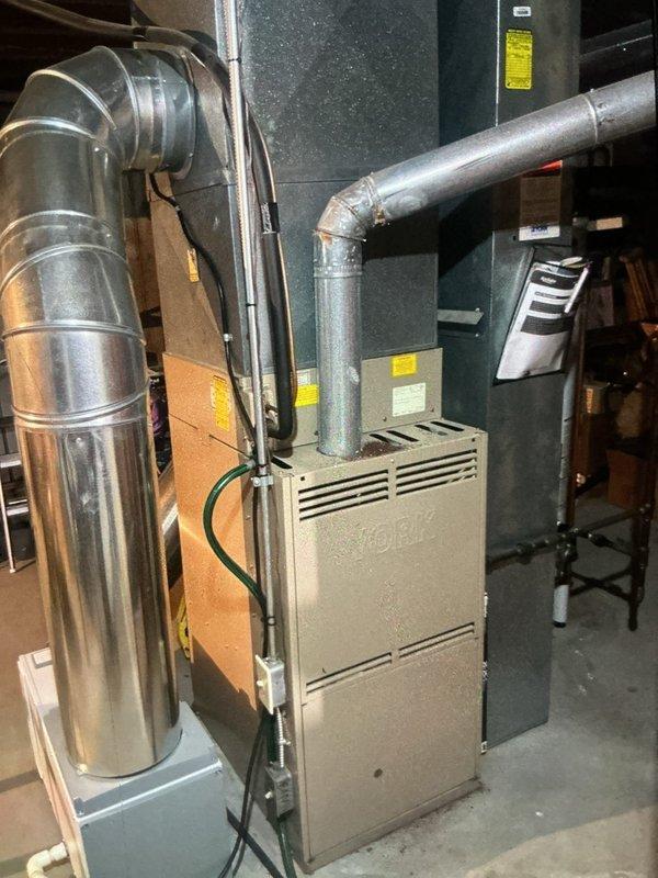 Completed HVAC system installation and diagnostic testing in mechanical room and attic space. Installed beige furnace unit with metallic ductwork components including curved aluminum ducts and galvanized steel piping with elbow joints. Mounted dark green air handler cabinet with wall-mounted control panel. In attic space, installed large evaporator coil unit with wire mesh screening and connected electrical control box. Attached diagnostic gauges displaying system readings and verified proper operation of all colored refrigerant lines and electrical connections.