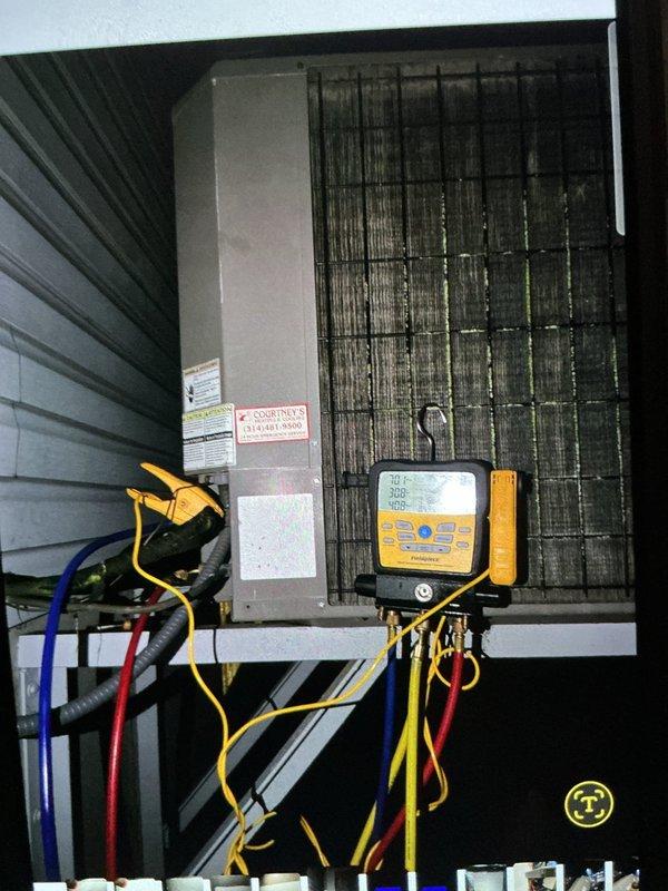 Completed HVAC system installation and diagnostic testing in mechanical room and attic space. Installed beige furnace unit with metallic ductwork components including curved aluminum ducts and galvanized steel piping with elbow joints. Mounted dark green air handler cabinet with wall-mounted control panel. In attic space, installed large evaporator coil unit with wire mesh screening and connected electrical control box. Attached diagnostic gauges displaying system readings and verified proper operation of all colored refrigerant lines and electrical connections.