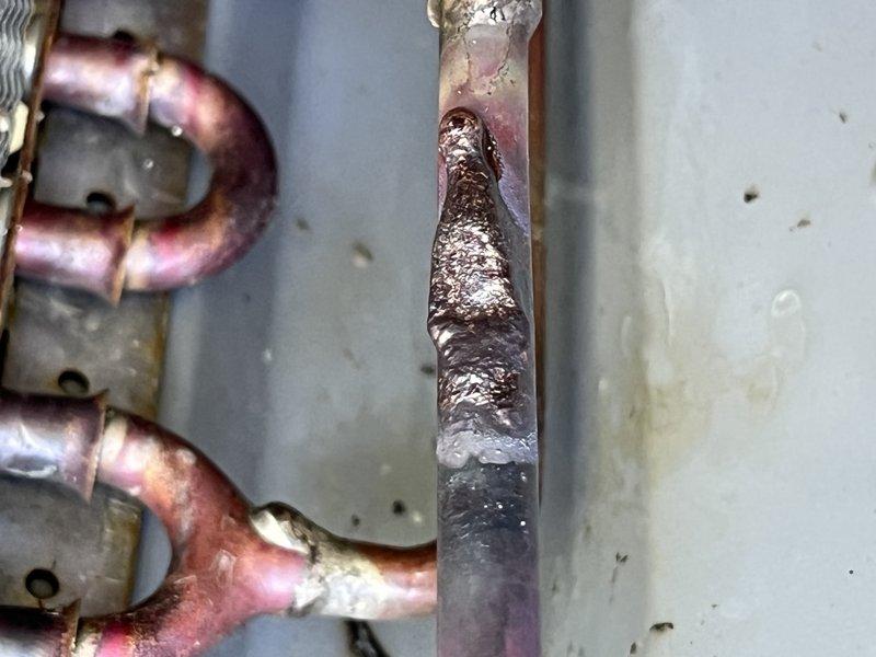 Responded to emergency no-cool call on 7-year-old Lennox system under warranty. Upon arrival, confirmed complete loss of cooling to entire residence. Performed diagnostic inspection of outdoor condensing unit and discovered severe corrosion on refrigerant line set, particularly on the liquid line connection. The corroded section exhibited advanced deterioration with rust buildup, flaking, and compromised integrity that would lead to refrigerant loss and system failure. Documented equipment condition with photos showing the extent of corrosion damage on copper refrigerant piping and mounting components. The corrosion pattern indicated prolonged exposure to moisture and environmental factors causing accelerated degradation of the line set. Identified unit model number 0720026-01/M-4383 during inspection. Given the severity of the line set corrosion and its impact on system performance, recommended replacement of affected refrigerant lines to restore proper operation and prevent future re