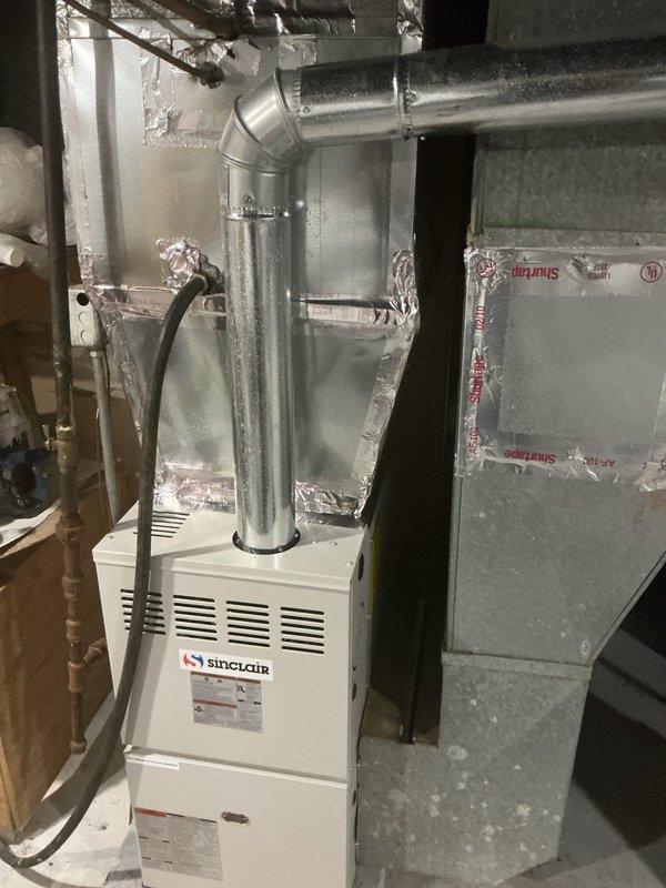 Responded to no-cooling complaint on 10+ year old residential AC system. Upon arrival, performed diagnostic evaluation of outdoor condenser unit showing significant weathering and rust deterioration on fan grille, and inspected indoor Sinclair furnace with air handler components in basement. Documented equipment condition through photographs revealing aging outdoor unit with corroded top grille assembly and indoor HVAC system configuration. System blowing air throughout home but failing to provide adequate cooling to living spaces.