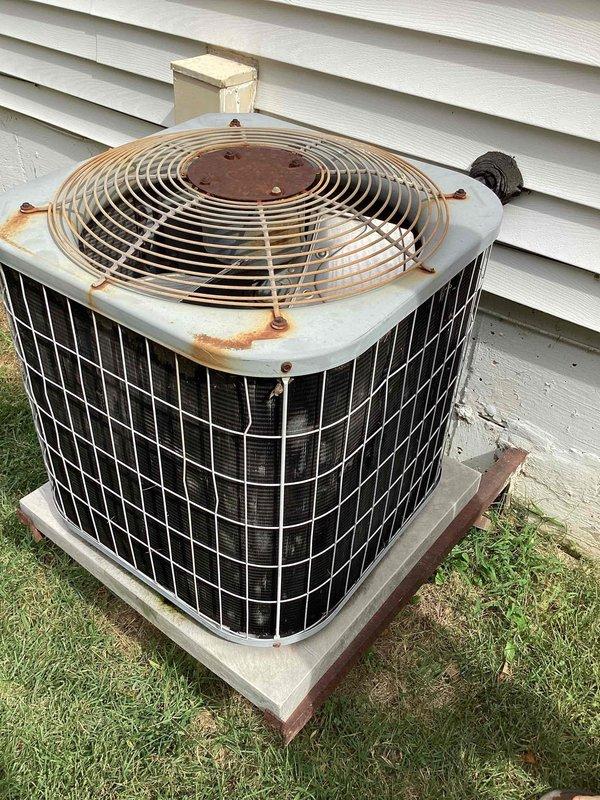 Responded to no cooling complaint following recent solar panel installation. Upon arrival, found thermostat displaying 81°F actual temperature while set to 69°F with a 2+ hour delay indicated. Performed diagnostic evaluation of 10+ year old outdoor condensing unit located on side of house. Unit showed significant age-related deterioration including rust staining on fan guard and top panel, indicating extended outdoor exposure. Conducted system assessment to determine if cooling issue was related to solar electrical work or equipment failure. Verified unit operation, checked electrical connections, and assessed refrigerant system performance. Documented equipment condition with photos showing thermostat readings and exterior unit condition for service records.