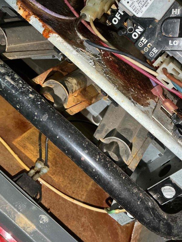 Responded to service call for sludge-like substance leaking from bottom of furnace unit. Upon inspection of Goodman furnace located in basement, discovered extensive rust and corrosion throughout internal components, including base plate, mounting surfaces, and electrical connection terminals. The heavy rust accumulation on metal surfaces and deteriorated condition of framework indicated prolonged moisture exposure, which was the source of the reported sludge material. Documented internal component condition with photographs showing corroded capacitors, control board connections, and compromised metal housing. Advised customer of significant corrosion affecting unit integrity and potential safety concerns related to electrical connections in deteriorated condition.