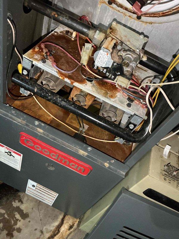 Responded to service call for sludge-like substance leaking from bottom of furnace unit. Upon inspection of Goodman furnace located in basement, discovered extensive rust and corrosion throughout internal components, including base plate, mounting surfaces, and electrical connection terminals. The heavy rust accumulation on metal surfaces and deteriorated condition of framework indicated prolonged moisture exposure, which was the source of the reported sludge material. Documented internal component condition with photographs showing corroded capacitors, control board connections, and compromised metal housing. Advised customer of significant corrosion affecting unit integrity and potential safety concerns related to electrical connections in deteriorated condition.