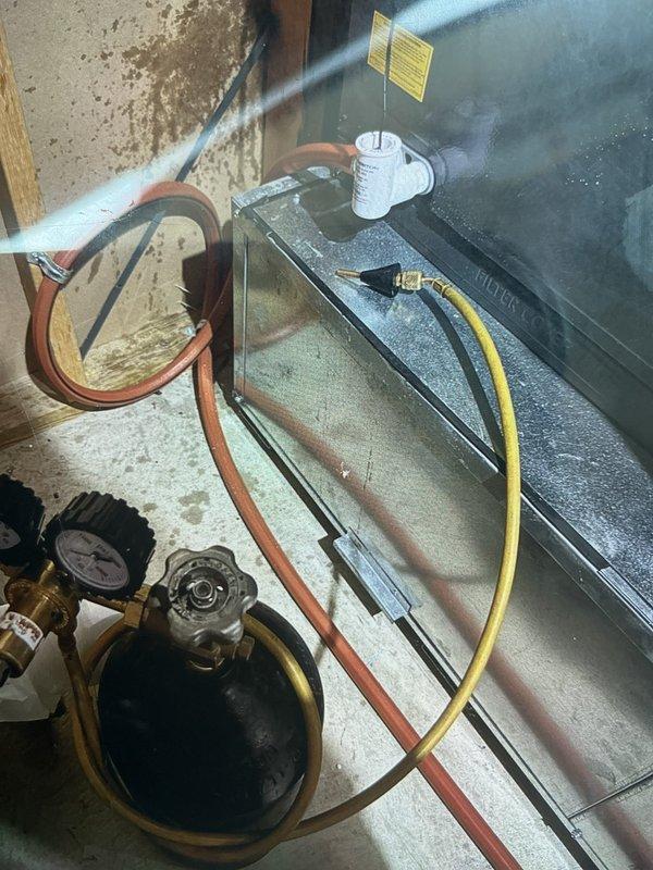 Responded to no cooling complaint on 2021 Rheem air conditioning system that had stopped working one week prior. Upon arrival, connected manifold gauge set to service ports and performed system diagnostics. Found evidence of significant water leakage on concrete floor beneath air handler, indicating drain line obstruction or secondary drain pan overflow. System was previously installed as part of complete furnace, AC, and coil replacement. Completed troubleshooting procedures, documented conditions with photographs showing gauge readings and water damage patterns, and restored cooling operation to unit located on side of residence at elevated position.