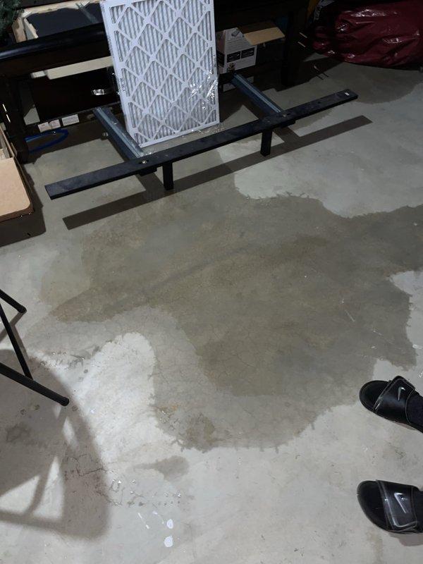 Responded to service callback regarding basement flooding that occurred during previous AC maintenance visit. Upon arrival, documented extensive water damage throughout basement area with visible pooling, moisture staining, and mineral deposits on concrete floor. Customer belongings showed water damage. Investigated source of flooding and inspected water supply connection at HVAC unit, locating blue flexible water line with shutoff valve in attic/crawl space above affected area. Photographed damage extent and plumbing connections for incident documentation. Verified current system operation and confirmed no active leaks present at time of callback inspection.