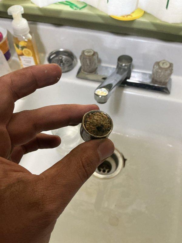 Responded to post-installation callback for low water pressure and popping noise at kitchen and bathroom sinks. Removed and cleaned faucet aerators which contained heavy mineral buildup and scale deposits causing restricted flow and noise. Inspected toilet tank which showed rust and mineral accumulation at base of flush valve assembly and interior surfaces; assessed condition and functionality of flush mechanism.