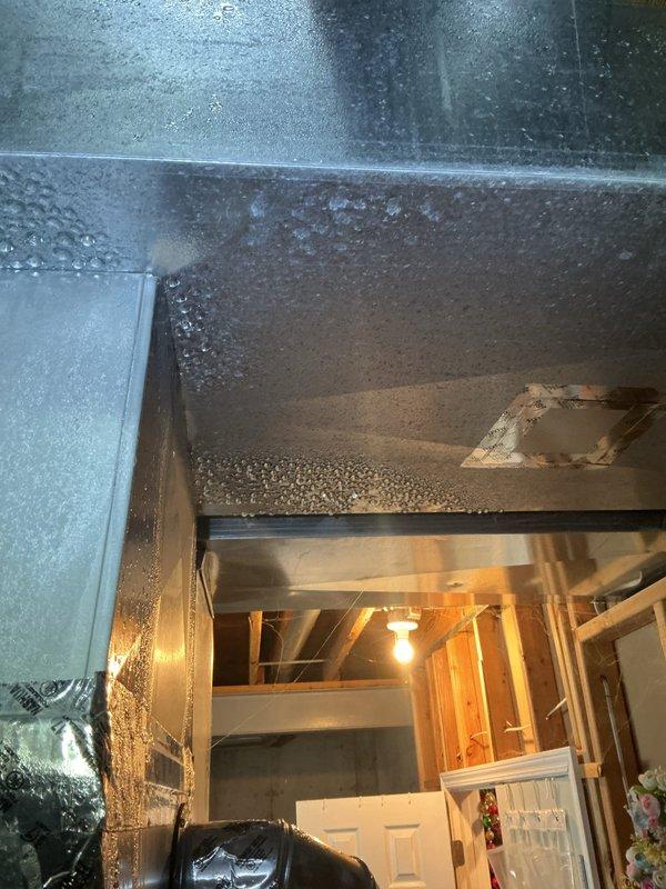 Responded to urgent service call for GF interlock system error code with blinking red indicator on recently installed HVAC unit less than one year old. Upon inspection, discovered severe condensation buildup throughout the system and surrounding ductwork in the mechanical area, indicating a critical indoor air quality issue. The excessive moisture accumulation on metallic surfaces and equipment suggested improper humidity control, inadequate ventilation, or potential drain line malfunction affecting the evaporator coil assembly. Inspected the 2025 model evaporator coil unit with heat exchanger grid, refrigerant line connections with brass valve fittings, and associated plumbing components. Documented extensive water droplet formation on ductwork and system components, which likely triggered the ground fault interlock safety mechanism due to moisture intrusion near electrical components. Photographed the coil face assembly and condensation conditions for warranty documentation purposes.