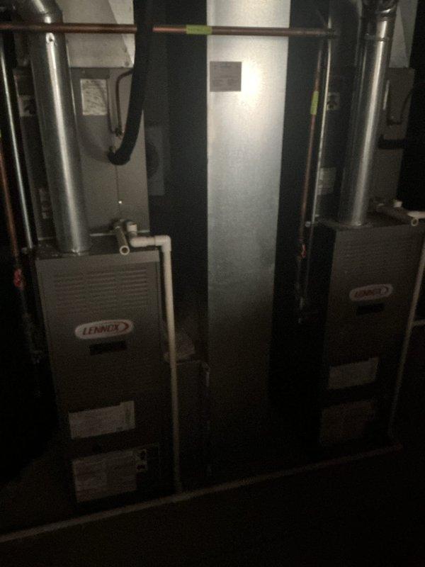 Responded to no cooling call for 20-year-old residential HVAC system. Upon arrival, performed diagnostic assessment of dual Lennox furnace installation in basement and exterior condenser units mounted on foundation. System was previously advised to be shut off due to cooling malfunction. Conducted visual inspection of indoor equipment, ductwork connections, and electrical components, then evaluated outdoor condenser units for operational issues. Documented equipment condition through photographic records showing both indoor furnace units with associated ductwork and piping, as well as exterior condenser placement and surrounding area conditions.