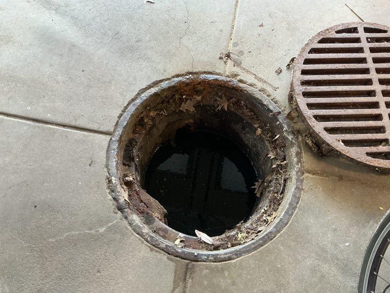 Responded to basement drainage issue where standing water was holding in a 2-foot drainage well accompanied by sewer gas odor. Upon inspection, found circular floor drain with heavily corroded metal rim and standing water in the basin. Assessed drainage system including adjacent rectangular grate drain. Documented existing conditions showing extensive rust on drain components, deteriorated concrete flooring with multiple cracks, and evidence of prolonged moisture exposure. Identified drainage well not actively backing up but failing to properly evacuate water, allowing sewer gases to escape into the basement area.