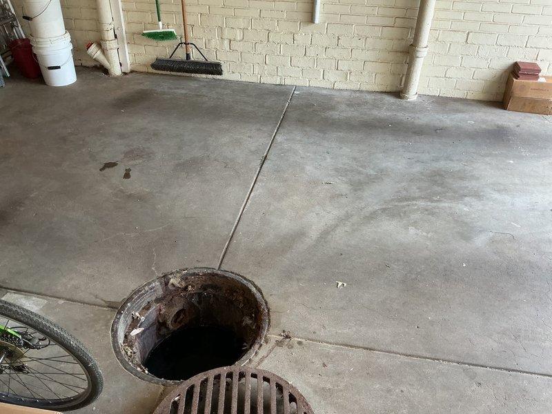 Responded to basement drainage issue where standing water was holding in a 2-foot drainage well accompanied by sewer gas odor. Upon inspection, found circular floor drain with heavily corroded metal rim and standing water in the basin. Assessed drainage system including adjacent rectangular grate drain. Documented existing conditions showing extensive rust on drain components, deteriorated concrete flooring with multiple cracks, and evidence of prolonged moisture exposure. Identified drainage well not actively backing up but failing to properly evacuate water, allowing sewer gases to escape into the basement area.