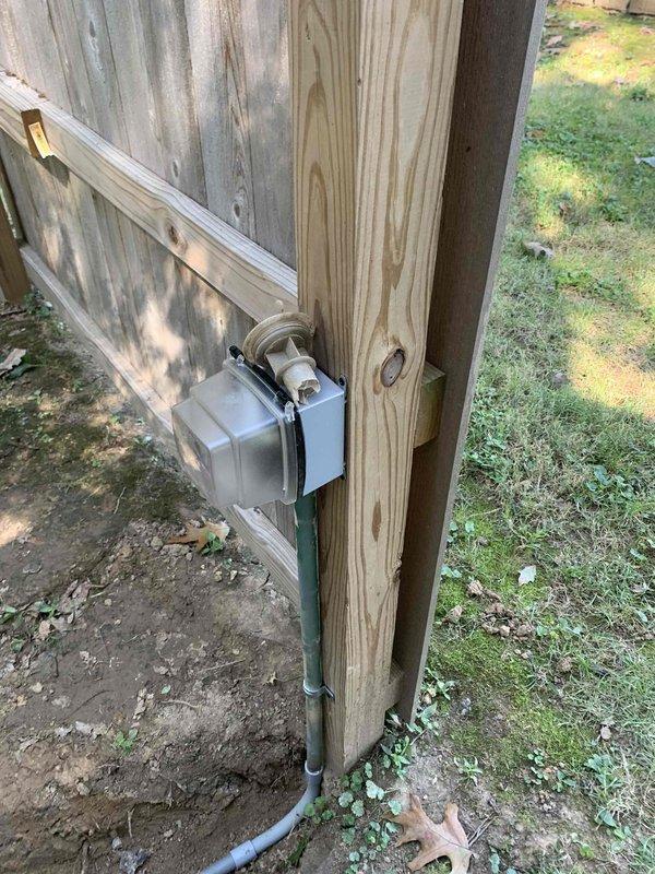 Relocated electrical service from existing shed-mounted installation to new fence post location. Installed weather-resistant meter box on wooden fence structure with proper mounting hardware and secured gray conduit running vertically along fence post to ground level. Routed electrical wiring through conduit system ensuring code-compliant installation and protection from environmental exposure. Verified all connections, tested system functionality, and confirmed proper grounding at new location.