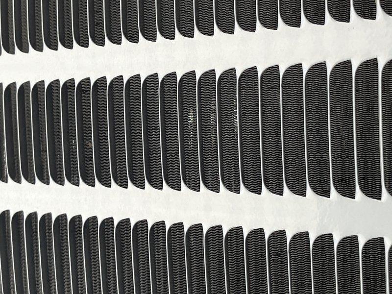 Responded to no cooling complaint with reported buzzing noise on 9-year-old system. Upon arrival, performed diagnostic evaluation of the outdoor condensing unit. Inspected condenser coil assembly and heat exchanger fins for proper airflow and operational integrity. Photographed coil condition showing parallel fin arrangement with uniform spacing and no visible damage or significant debris accumulation. Verified fin structure and spacing throughout multiple rows of the heat exchanger assembly. System evaluated for buzzing source and cooling capacity issues affecting entire HVAC operation.