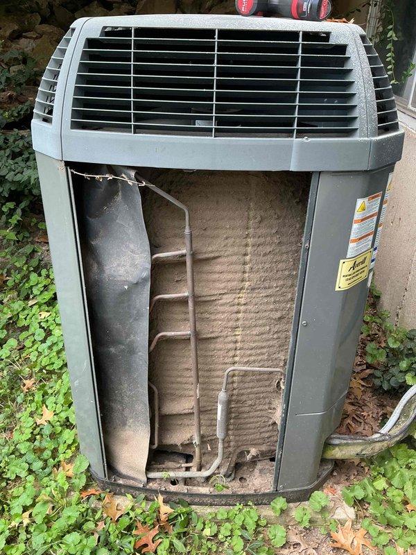 Responded to no-cooling complaint on 8-year-old Trane whole-house air conditioning system. Upon inspection, found outdoor condenser unit with significant dirt, dust, and debris accumulation on condenser coils and aluminum fins. Removed front access panel to assess internal components and refrigerant lines. Condenser coil showed heavy buildup restricting airflow through finned surfaces, which was likely contributing to reduced cooling capacity and system inefficiency. All copper refrigerant lines and connections appeared intact with no visible signs of leakage or damage. Unit structure and housing in acceptable condition for age. Documented internal component condition with photographs showing extent of coil contamination and overall system state for maintenance records.