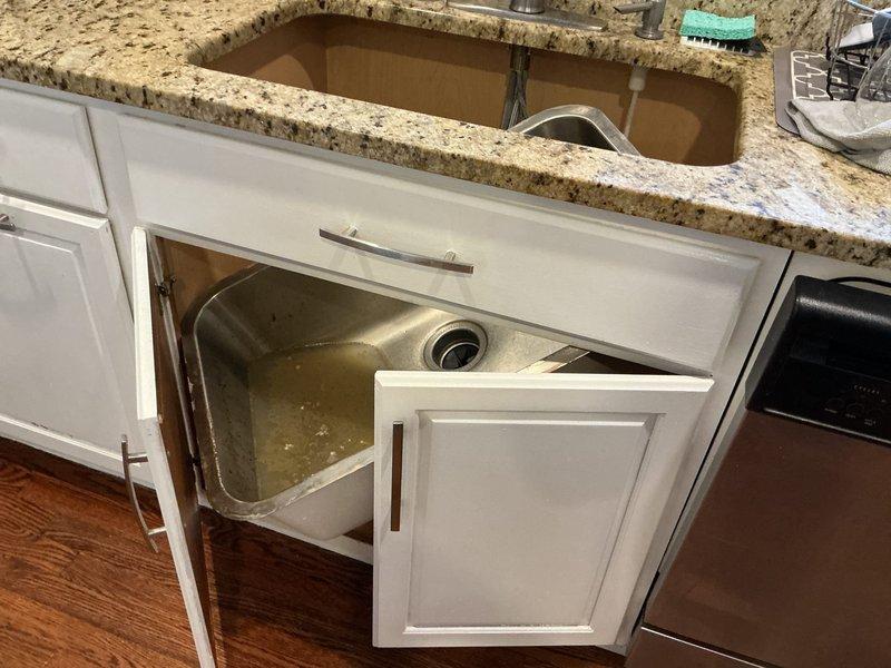 Responded to kitchen plumbing issue involving non-functional garbage disposal and clogged kitchen sink. Upon arrival, found standing water in undermount stainless steel sink basin with drainage backup. Accessed cabinet space beneath granite countertop to inspect plumbing connections, drain assembly, and disposal unit. Removed sink from mounting position to access drainage system and disposal connections. Cleared obstruction from drain line and verified proper water flow through drainage pipes. Inspected supply lines and P-trap assembly for additional blockages or damage. Tested garbage disposal functionality and restored sink to proper mounting position under countertop. Verified all plumbing connections were secure and system was operating correctly with no leaks.