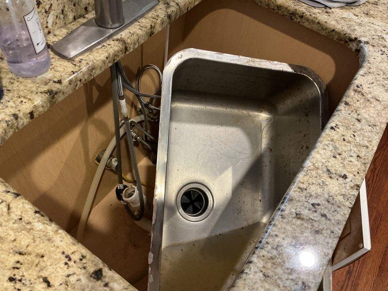 Responded to kitchen plumbing issue involving non-functional garbage disposal and clogged kitchen sink. Upon arrival, found standing water in undermount stainless steel sink basin with drainage backup. Accessed cabinet space beneath granite countertop to inspect plumbing connections, drain assembly, and disposal unit. Removed sink from mounting position to access drainage system and disposal connections. Cleared obstruction from drain line and verified proper water flow through drainage pipes. Inspected supply lines and P-trap assembly for additional blockages or damage. Tested garbage disposal functionality and restored sink to proper mounting position under countertop. Verified all plumbing connections were secure and system was operating correctly with no leaks.