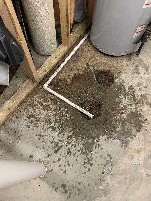 Responded to recurring basement water backup issue with floor drain inspection and assessment. Upon arrival, found evidence of recent water accumulation on concrete floor surrounding multiple floor drains, with visible staining and moisture damage indicating backup had occurred. Inspected drain openings and observed corrosion around drain perimeters. Documented conditions showing water staining patterns near water heater and throughout utility area floor surface, confirming drainage system failure requiring further intervention to resolve underlying blockage or structural issue causing repeated backups.