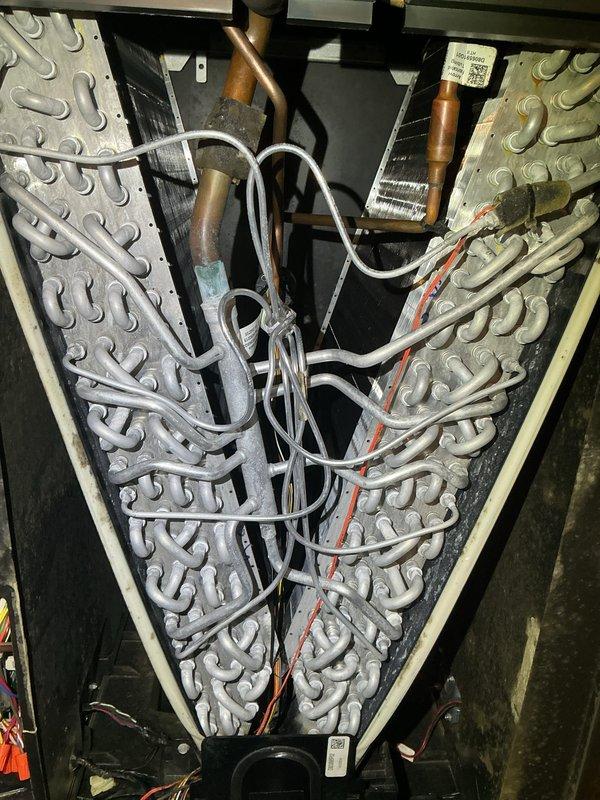 Performed comprehensive AC tune-up on 26-year-old York system per customer request based on thermostat reminder. Inspected evaporator coil assembly showing V-configuration with serpentine tubing arrangement, confirmed refrigerant lines and electrical connections secure with no visible leaks or damage. Accessed air handler unit in attic space, examined heating coil assembly and housing, noted minor dust accumulation typical for system age but overall components functioning properly with no immediate service concerns identified.