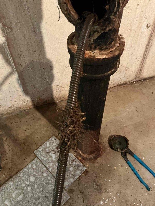 Responded to callback for persistent slow draining and backup issues in basement drain system that had been previously serviced approximately two weeks prior. Upon inspection, identified severely deteriorated cast iron vertical stack with extensive corrosion throughout the pipe assembly, particularly at connection points and floor penetration. The advanced rust and oxidation present on the main stack, combined with visible water staining on the concrete floor around the pipe base, indicated the recurring drainage problems were likely caused by interior pipe deterioration and potential blockage from rust scale buildup rather than a simple clog. 

Assessed the horizontal PVC branch connections tied into the corroded cast iron stack and determined the aging infrastructure was contributing to the ongoing drainage issues. The condition of the piping suggests the previous clearing provided only temporary relief, as the compromised pipe interior continues to catch debris and restrict flow. Do