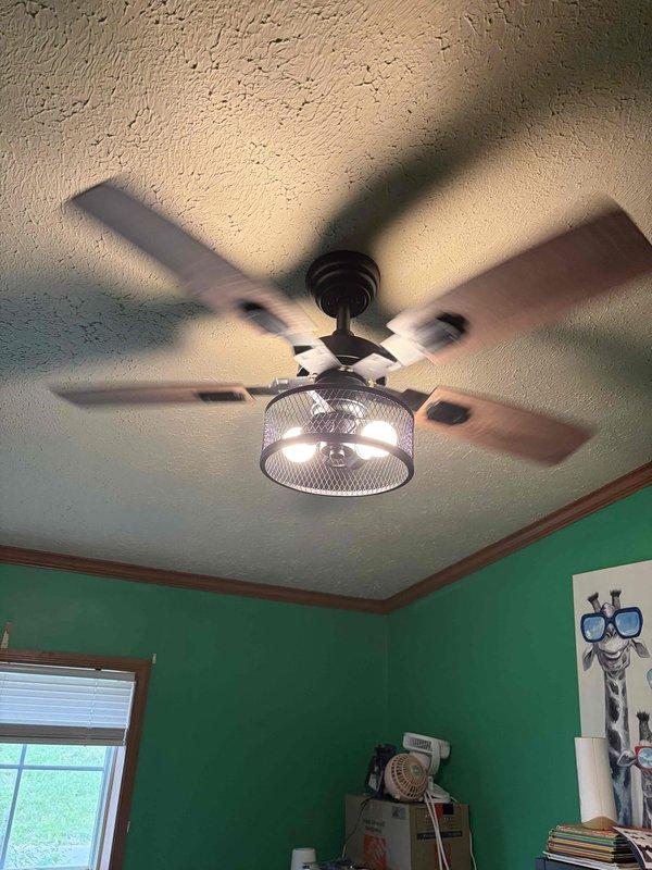 Completed installation of three ceiling fans in residential property. First unit installed features bronze finish with integrated cage-style light fixture and five-blade configuration, mounted in bedroom with textured ceiling. Second unit consists of traditional chandelier-style fixture with multiple candle bulbs, chain-mounted in kitchen/dining area with crown molding. Verified proper electrical connections, tested fan operations at all speed settings, and confirmed lighting functionality on both fixtures. All installations secured to ceiling joists per manufacturer specifications and local electrical code requirements.