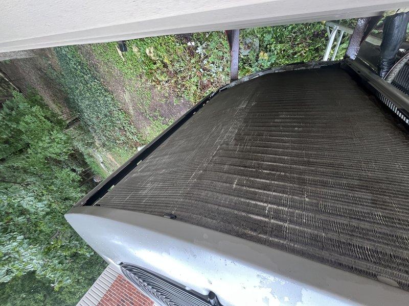 Responded to no cooling complaint with "GFHS I sense open" fault displayed on Lennox programmable digital thermostat. Upon arrival, accessed property using provided entry code and inspected system components. Examined outdoor condensing unit located beneath deck structure and found evaporator coils heavily soiled with dirt, dust, and debris accumulation causing restricted airflow. Opened access panel to assess coil condition and confirmed significant buildup across fin surfaces with visible streaking and discoloration. Verified thermostat fault related to system sensor issue on approximately 10-year-old unit originally installed by Classic Aire Care. Documented equipment condition with photographs showing extent of coil contamination and moisture present on unit housing, indicating recent system operation attempts prior to service call.