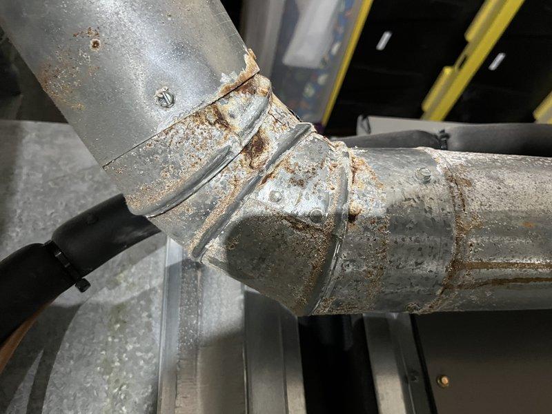 Responded to no heat call where system fan was operating but furnace failed to ignite. Upon inspection, discovered severely corroded ductwork and pipe connections with extensive rust damage at joints and elbow fittings, indicating prolonged moisture exposure that compromised system integrity. Documented deteriorated galvanized metal components and rust accumulation around coupling areas; recommended immediate replacement of affected ductwork sections to restore proper heating function and prevent further system degradation.