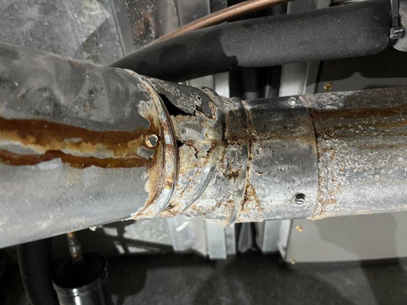 Responded to no heat call where system fan was operating but furnace failed to ignite. Upon inspection, discovered severely corroded ductwork and pipe connections with extensive rust damage at joints and elbow fittings, indicating prolonged moisture exposure that compromised system integrity. Documented deteriorated galvanized metal components and rust accumulation around coupling areas; recommended immediate replacement of affected ductwork sections to restore proper heating function and prevent further system degradation.