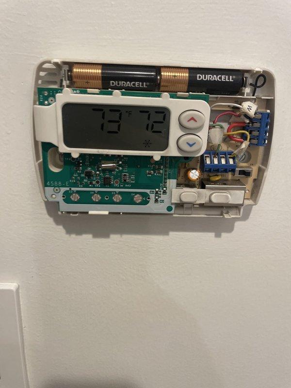 Responded to service call for malfunctioning thermostat controlling two 9-year-old HVAC units located in basement. Upon arrival, inspected White-Rodgers digital thermostat displaying 72°F in cooling mode. Removed cover to perform diagnostic evaluation of internal components, checking battery condition, circuit board integrity, and terminal wiring connections. Verified proper installation of Duracell AA batteries with secure spring contacts. Examined green circuit board (model 4588) for any signs of component failure or damage. Inspected all wire terminations at terminal block, confirming red, white, and blue wires were properly seated in connector tabs. Tested thermostat functionality and temperature control buttons to ensure proper communication with HVAC system. Documented equipment condition with photographs showing both exterior and interior components for service records.