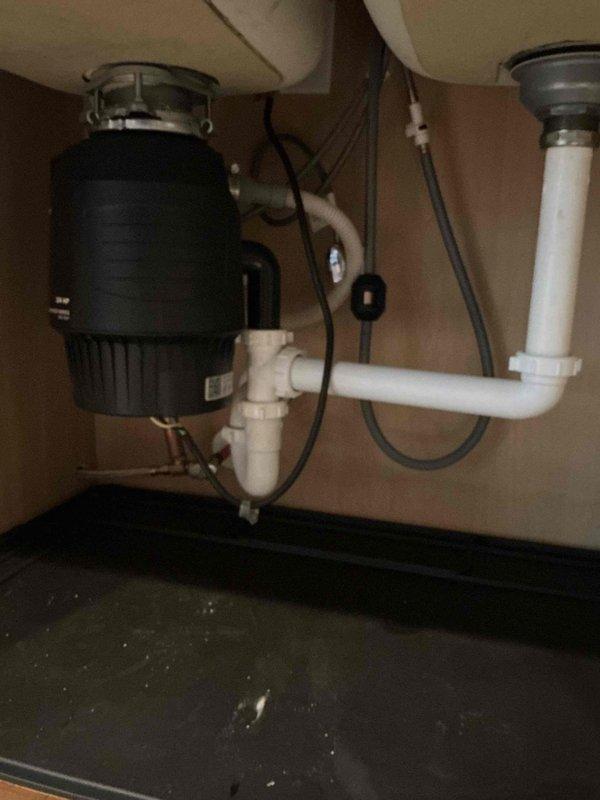 Responded to service call for kitchen sink producing gurgling sounds during drainage. Upon inspection, confirmed sink was draining properly with no standing water or slow drainage issues. Examined the double-bowl undermount sink configuration with garbage disposal installed on one basin. Inspected under-sink plumbing including disposal unit, P-trap assembly, and PVC drain connections. Gurgling noise typically indicates a venting issue or partial blockage in the drainage system allowing air to be pulled through the trap. Verified all visible connections were secure and properly configured. Documented existing plumbing setup with disposal unit and dual drain system for service records.