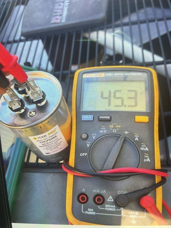 Responded to callback for non-operational outdoor unit with condenser fan failure and warm air discharge. Upon arrival, performed diagnostic testing on the dual-run capacitor using Fluke 115 multimeter. Initial capacitance reading measured 45.3 microfarads on common terminal, significantly below manufacturer specifications. Secondary testing confirmed capacitor failure with reading of 577 microfarads out of acceptable range. Identified failed TITAN brand capacitor as root cause of condenser fan motor failure and system malfunction. Replaced defective dual-run capacitor with properly rated OEM equivalent component. Restored power to system and verified condenser fan motor operation and proper amp draw. Confirmed unit cycling correctly with adequate airflow and temperature differential across evaporator coil. System returned to normal cooling operation with all components functioning within specifications.