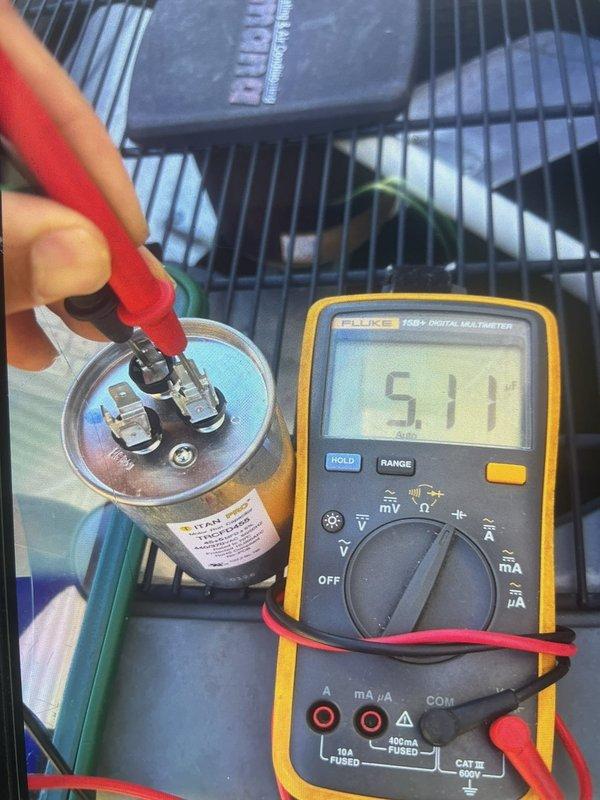 Responded to callback for non-operational outdoor unit with condenser fan failure and warm air discharge. Upon arrival, performed diagnostic testing on the dual-run capacitor using Fluke 115 multimeter. Initial capacitance reading measured 45.3 microfarads on common terminal, significantly below manufacturer specifications. Secondary testing confirmed capacitor failure with reading of 577 microfarads out of acceptable range. Identified failed TITAN brand capacitor as root cause of condenser fan motor failure and system malfunction. Replaced defective dual-run capacitor with properly rated OEM equivalent component. Restored power to system and verified condenser fan motor operation and proper amp draw. Confirmed unit cycling correctly with adequate airflow and temperature differential across evaporator coil. System returned to normal cooling operation with all components functioning within specifications.
