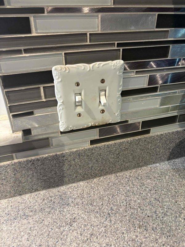 Inspected and tested double light switch and outlet as reported. Verified proper operation of decorative double toggle switch mounted on kitchen backsplash and adjustable spotlight fixture. All electrical components functioning correctly with no replacement necessary.