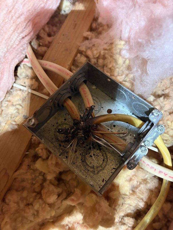 Responded to electrical service call for fixture installation and junction box repair in attic space. Upon inspection, discovered severely damaged junction box with charred wiring and burn marks indicating previous electrical malfunction or overheating condition. Multiple wire connections showed heat damage with darkened debris present inside the metal enclosure, creating immediate safety hazard.

Removed compromised junction box and damaged wiring. Installed new electrical junction box with proper wire connections using approved wire nuts and connectors. Ensured all electrical connections were secure and met code requirements. Routed new electrical cables through attic space, securing yellow cable runs and maintaining proper clearances from insulation materials. Connected black, white, and ground wires according to electrical standards.

Verified all connections were tight and properly insulated. Confirmed junction box was securely mounted to structural framing members. Repositioned p