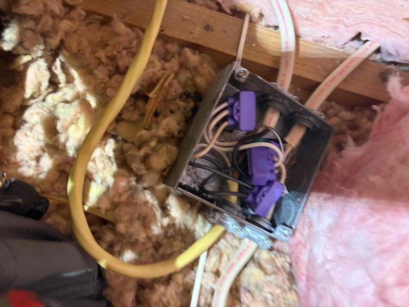 Responded to electrical service call for fixture installation and junction box repair in attic space. Upon inspection, discovered severely damaged junction box with charred wiring and burn marks indicating previous electrical malfunction or overheating condition. Multiple wire connections showed heat damage with darkened debris present inside the metal enclosure, creating immediate safety hazard.

Removed compromised junction box and damaged wiring. Installed new electrical junction box with proper wire connections using approved wire nuts and connectors. Ensured all electrical connections were secure and met code requirements. Routed new electrical cables through attic space, securing yellow cable runs and maintaining proper clearances from insulation materials. Connected black, white, and ground wires according to electrical standards.

Verified all connections were tight and properly insulated. Confirmed junction box was securely mounted to structural framing members. Repositioned p