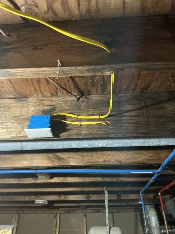 Completed electrical rewiring installation in unfinished attic/ceiling space with exposed joists and framing. Installed new yellow electrical cable routing across ceiling joists, mounted junction box to structural beam, and ran white electrical wiring perpendicular to framing members in accordance with code requirements for the approved estimate.