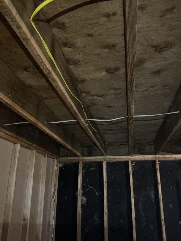 Completed electrical rewiring installation in unfinished attic/ceiling space with exposed joists and framing. Installed new yellow electrical cable routing across ceiling joists, mounted junction box to structural beam, and ran white electrical wiring perpendicular to framing members in accordance with code requirements for the approved estimate.