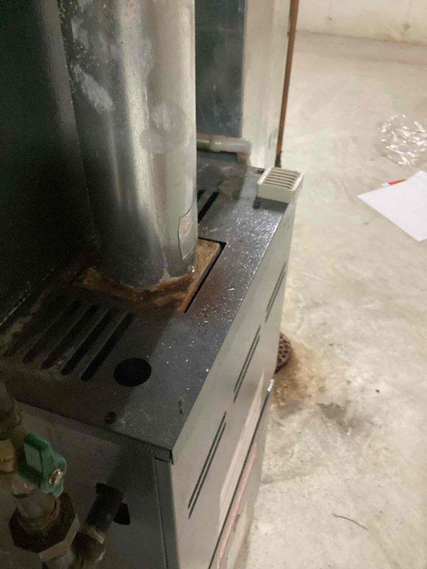 Responded to service call for reported cracks in furnace exhaust on unit over 10 years old located in basement. Upon inspection, identified significant rust and corrosion at the flue pipe connection point where the vertical exhaust duct meets the furnace cabinet, confirming customer's carbon monoxide safety concerns. Documented conditions with photographs showing deteriorated pipe-to-equipment junction with brown/orange oxidation at the base of the exhaust penetration. Recommended immediate repair or replacement of compromised exhaust components to ensure safe operation and prevent potential CO exposure.