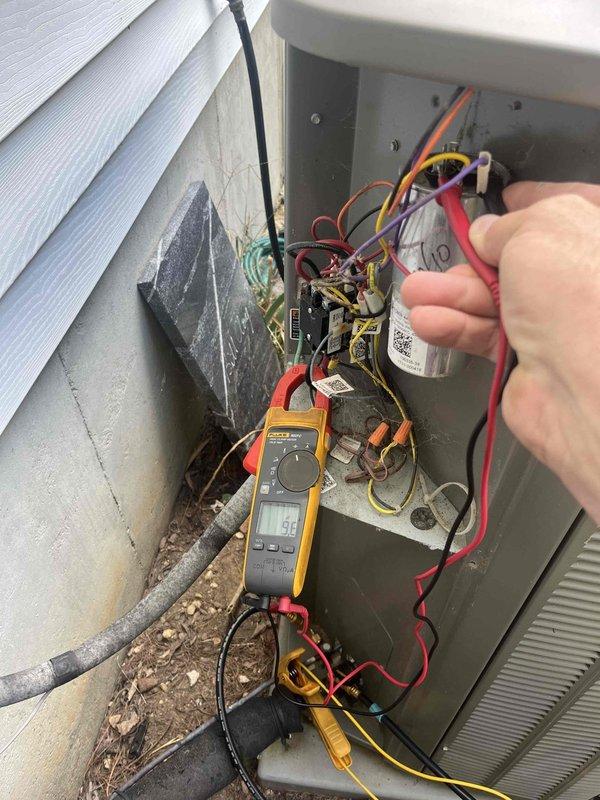 Responded to callback for an AC system not cooling. Inspected the outdoor condenser and found the coil fins coated with dirt, dust, and leaf debris, restricting airflow. Opened the electrical compartment and performed electrical diagnostics on the run capacitor and contactor using a clamp meter, noting loose, unterminated wire ends and cobweb debris in the control section. Documented findings with photos and recommended coil cleaning and wiring/component repairs to restore proper cooling operation.