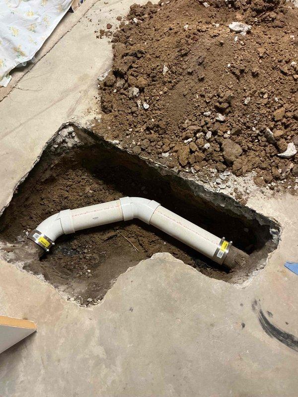 Broke out and excavated a section of the basement concrete slab to expose the deteriorated cast iron sewer lateral, then removed the corroded pipe and replaced it with new Schedule 40 PVC pipe and fittings, connected to the existing lines with band-style couplings. Backfilled the trench, restored the slab with concrete to a rough finish, and hauled away excess spoils.
