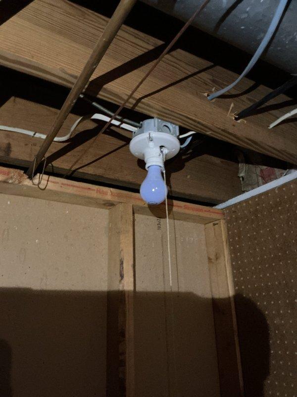 Performed a comprehensive electrical inspection of the basement area, including exposed wiring, junction boxes, and lighting fixtures. Observed pull-chain porcelain and bare-bulb fixtures mounted to surface junction boxes, with non-metallic and metal-sheathed cabling routed along the floor joists and several loose, unsecured conductors near the fixture locations. Documented the condition of the wiring and fixtures with photographs for the service record.