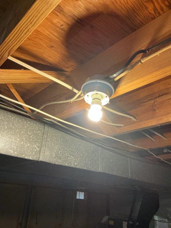 Performed a comprehensive electrical inspection of the basement area, including exposed wiring, junction boxes, and lighting fixtures. Observed pull-chain porcelain and bare-bulb fixtures mounted to surface junction boxes, with non-metallic and metal-sheathed cabling routed along the floor joists and several loose, unsecured conductors near the fixture locations. Documented the condition of the wiring and fixtures with photographs for the service record.