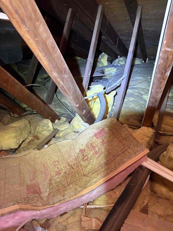 Inspected the ductless mini split reported for leaking and poor operation, accessing the attic to evaluate the condensate drain line, drain routing, and surrounding insulation for moisture intrusion and water damage. Documented displaced and water-stained insulation along the condensate path and the affected ceiling area for follow-up repairs.