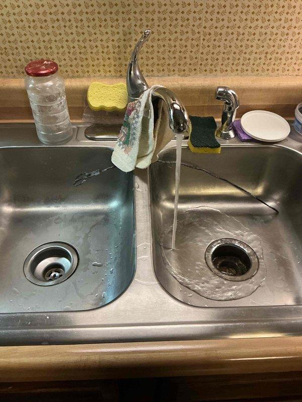 Responded to a clogged double-basin kitchen sink and inspected the under-sink PVC drain assembly, including the slip-nut joints and P-trap, for restrictions. Cleared the blockage from the drain line, restoring free flow, and verified proper drainage from both basins with sustained running water and no leaks at the trap connections.