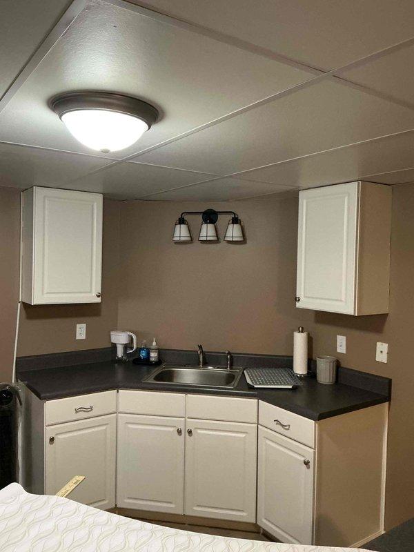 Performed an on-site estimate for new light fixture installation in a kitchenette area, assessing the existing flush-mount ceiling fixture in the drop ceiling and the three-light vanity-style fixture above the sink, along with nearby switch and receptacle locations. Documented existing conditions and confirmed no visible damage or code concerns, with the work scope prepared for fixture replacement.