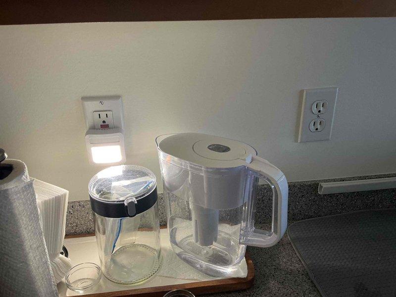 Performed an on-site estimate for new light fixture installation in a kitchenette area, assessing the existing flush-mount ceiling fixture in the drop ceiling and the three-light vanity-style fixture above the sink, along with nearby switch and receptacle locations. Documented existing conditions and confirmed no visible damage or code concerns, with the work scope prepared for fixture replacement.