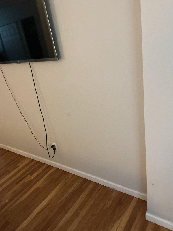 Performed troubleshooting of a wall-mounted television installation, inspecting the outlet and concealed wiring path behind the wall to diagnose the reported issue. Evaluated the receptacle and connected cord at the baseboard outlet and checked adjacent wall surfaces for signs of damage or interference. Documented existing conditions with photos.