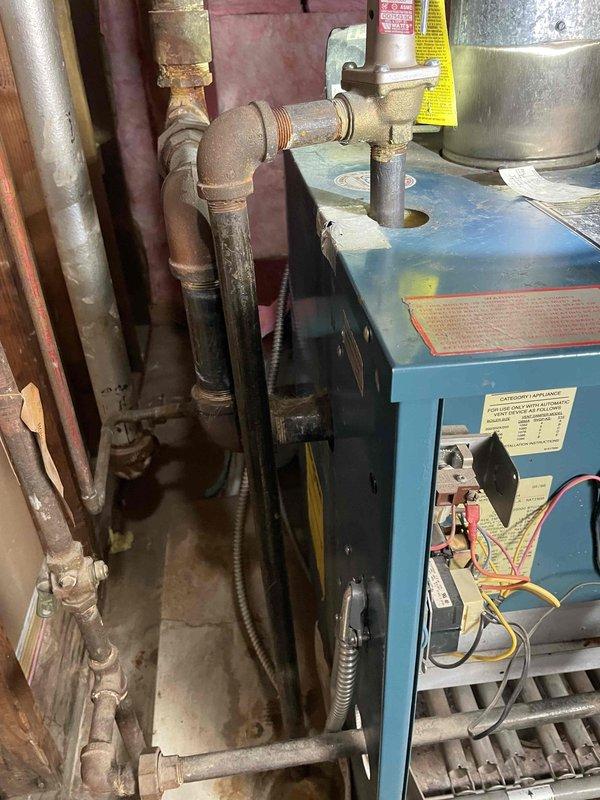 Responded to a no-heat call on a boiler that made loud noises and began leaking after the water supply was shut off and restored. Inspected the unit and found heavy corrosion and mineral buildup on the supply and return piping, valves, and fittings, with the temperature/pressure gauge reading low system pressure and temperature. Documented the system condition and leak points with photos for repair evaluation.