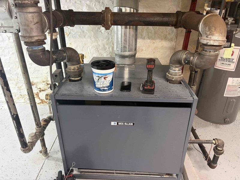 Performed a seasonal heating tune-up on a Weil-McLain boiler serving the hydronic radiator system, including inspection of the boiler, flue venting, and supply/return piping and fittings. Noted surface rust and corrosion on the threaded iron pipe joints and fittings, which should be monitored for leaks. Reviewed radiator operation with the homeowner, including how to turn the radiator valves on and off, to ensure proper heat control throughout multiple rooms.