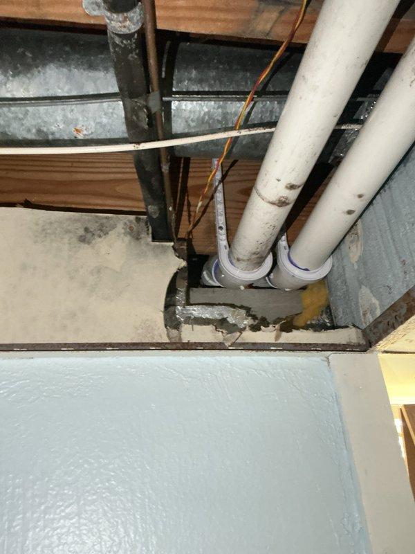 Inspected the 2-year-old A/C system in response to reported mold and moisture damage, and examined the exposed ceiling cavity where the supply ductwork and condensate drain piping run. Observed dark mold-like staining and moisture damage on the ceiling drywall directly beneath the galvanized duct and condensate drain line penetration, with torn duct wrap and disturbed insulation and patching at the opening. Documented the affected areas with photos and identified the condensate drain and duct insulation/penetration area as the probable moisture source.